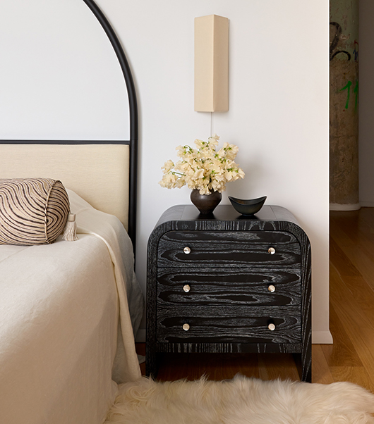 Custom curved three-drawer bedside table by Laurie Blumenfeld with a noir textured wood finish and round hardware.