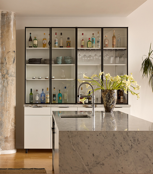 Custom kitchen hutch designed by Laurie Blumenfeld with glass and metal doors, white lacquer cabinetry, and marble, complementing a stone kitchen island.